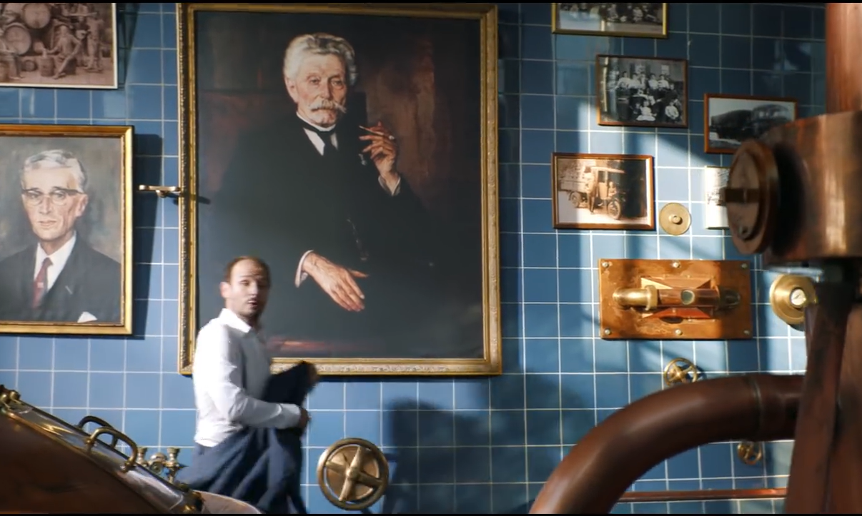 Interieur van een brouwerij met portretten en koperen apparatuur op blauw betegelde muur.