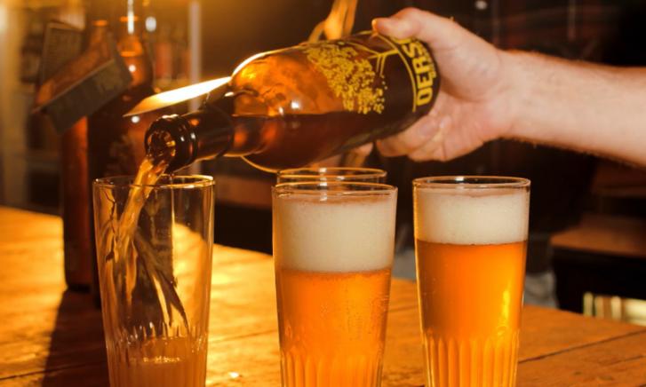 Een fles Oersoep bier voor een rij biertaps met gele tekst 