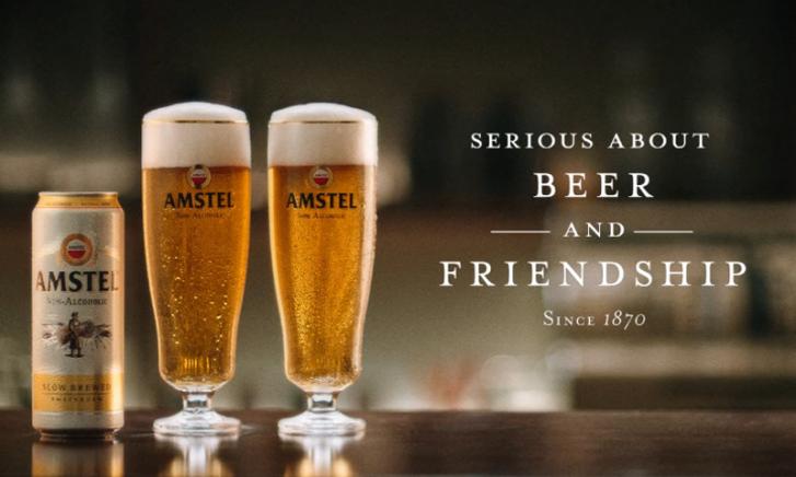 Twee mannen proosten met Amstel bier in een drukke buitenomgeving.