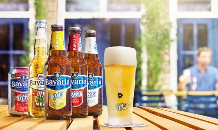 Bavaria 0.0% bieren op een houten tafel, met mensen op de achtergrond.
