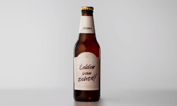 Man met hoed en bril drinkt bier en heeft een schuimsnor, Amstelglas zichtbaar.