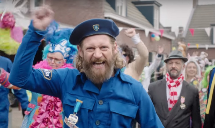 Man in blauw carnavalskostuum in een bar met Bavaria op de achtergrond.