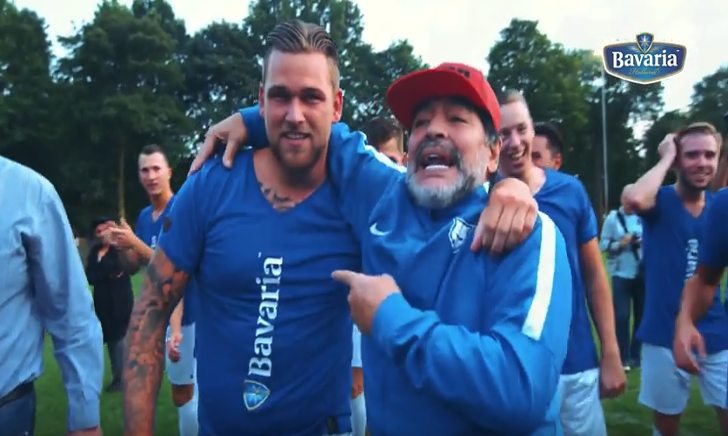 Groep mensen in blauwe sportkleding poseert voor een doel met Bavaria banners.