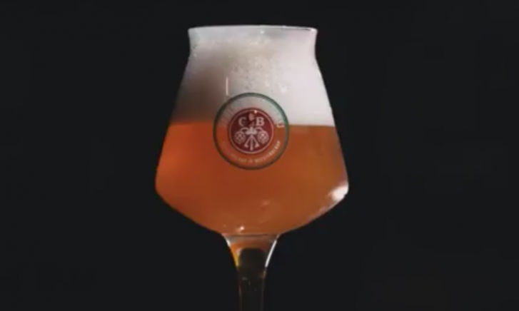 Man houdt een glas Grolsch bier omhoog in gedimde verlichting.