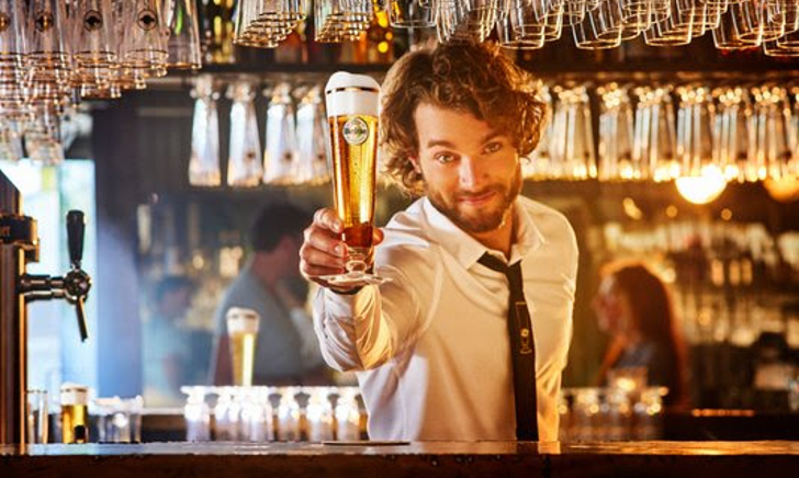 Glas Warsteiner bier wordt ingeschonken, branding zichtbaar.