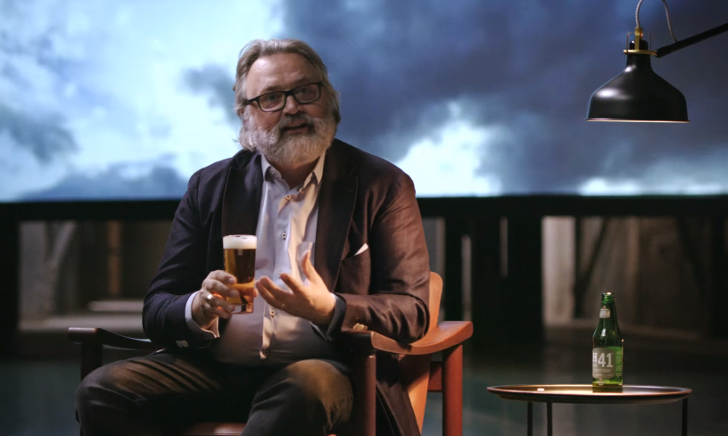 Een fles Heineken Wild Lager H41 naast een leeg glas op een donkere achtergrond.