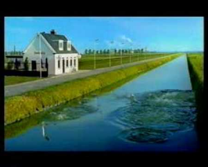 Duikboot varend door een smal kanaal naast een gebouw en een weg.