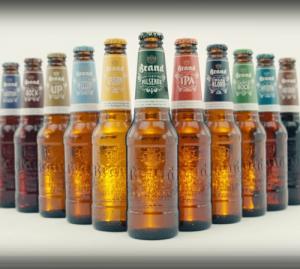 Man houdt een glas bier vast op een zonnig terras met mensen op de achtergrond.