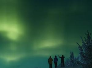 Drie mensen in blauwe overalls kijken door een raam naar een ruimtewandelaar.