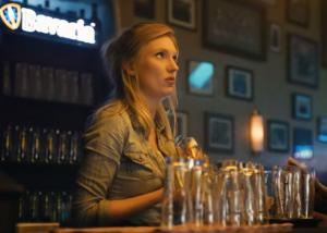 Biertap schenkt helder bier in een schuin glas met merklogo op de achtergrond.