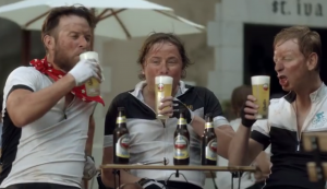 Twee mannen lossen dranken uit een busje voor een historisch hotel in een zonnig dorpsplein.