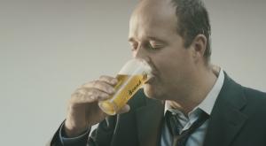 Man in bruine jas plaatst flesjes in een koelkast naast een krat bier.