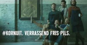 Een fles en glas Grolsch Kornuit bier op een houten tafel met hopbellen.