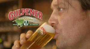 Twee mensen in een bar proosten met glazen bier voor een rek vol flessen.