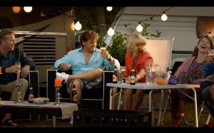 Man in een blauwe blouse drinkt een glas Amstel bier in een tuin setting.