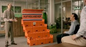 Vier mannen in een kantoor kijken naar een oranje bouwsel van bierkratten.