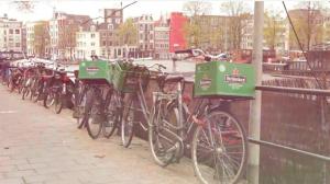 Twee mannen lachen en wijzen naar een fietskrat met Heineken logo buiten.